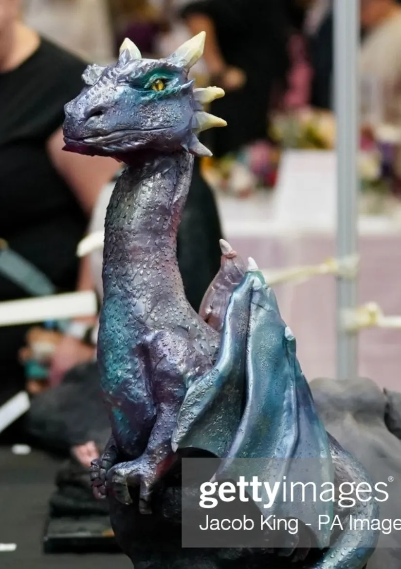 Sculpted iridescent dragon cake with purple and teal scales, horns, and folded wings