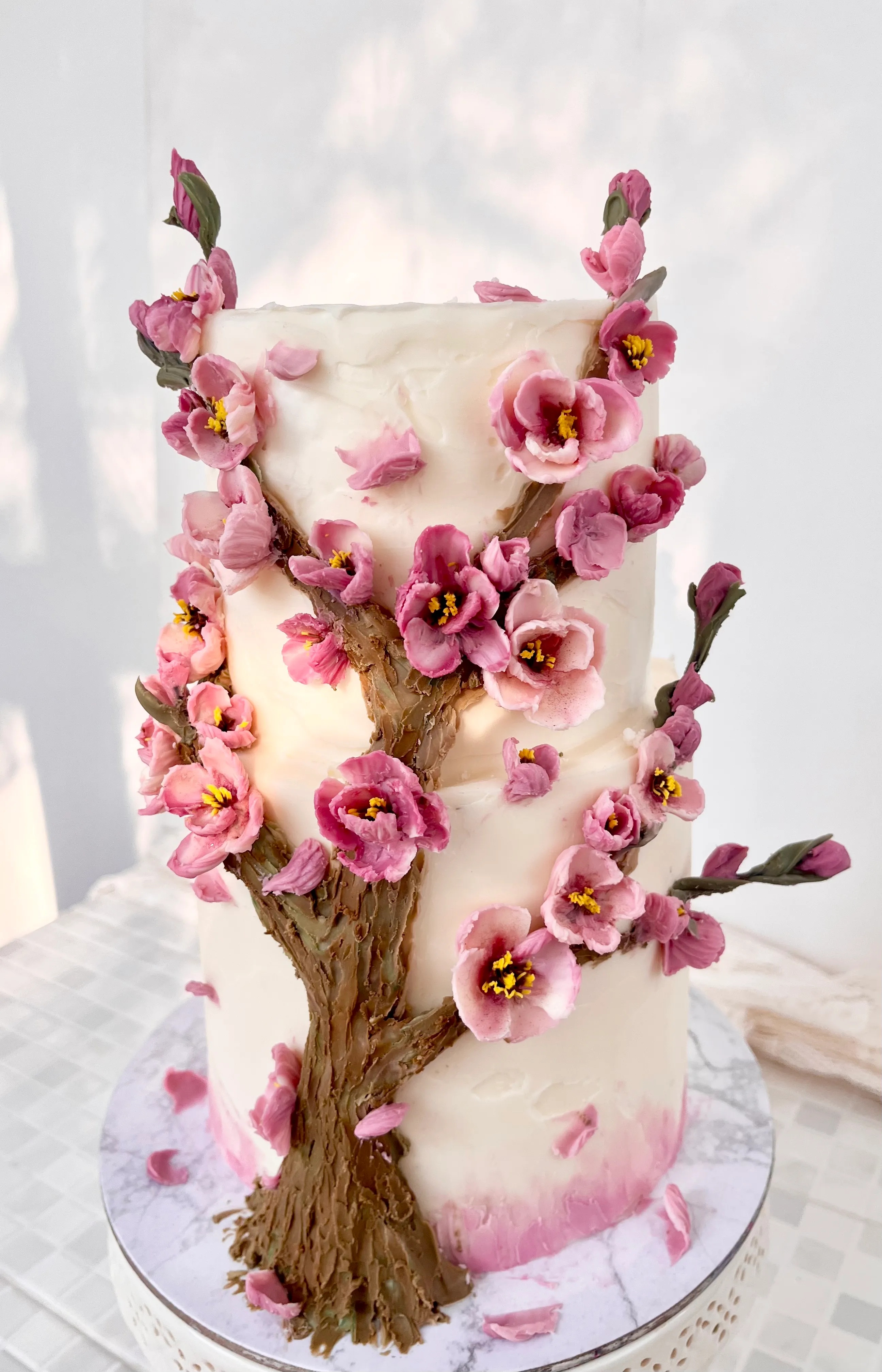 Two-tier white buttercream cake with a sculpted cherry blossom tree and dozens of handcrafted pink flowers