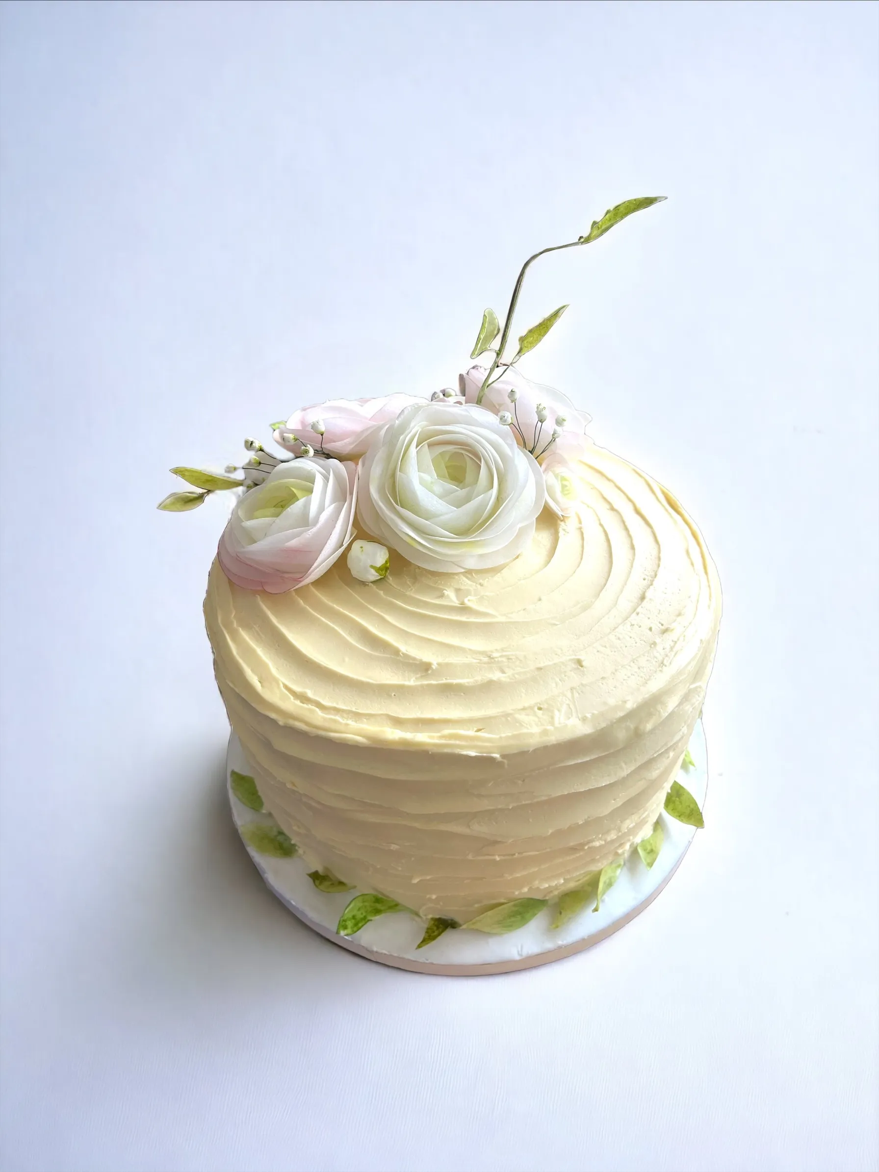 Single-tier cake with textured ivory buttercream swirls topped with white and pale pink sugar roses and baby's breath