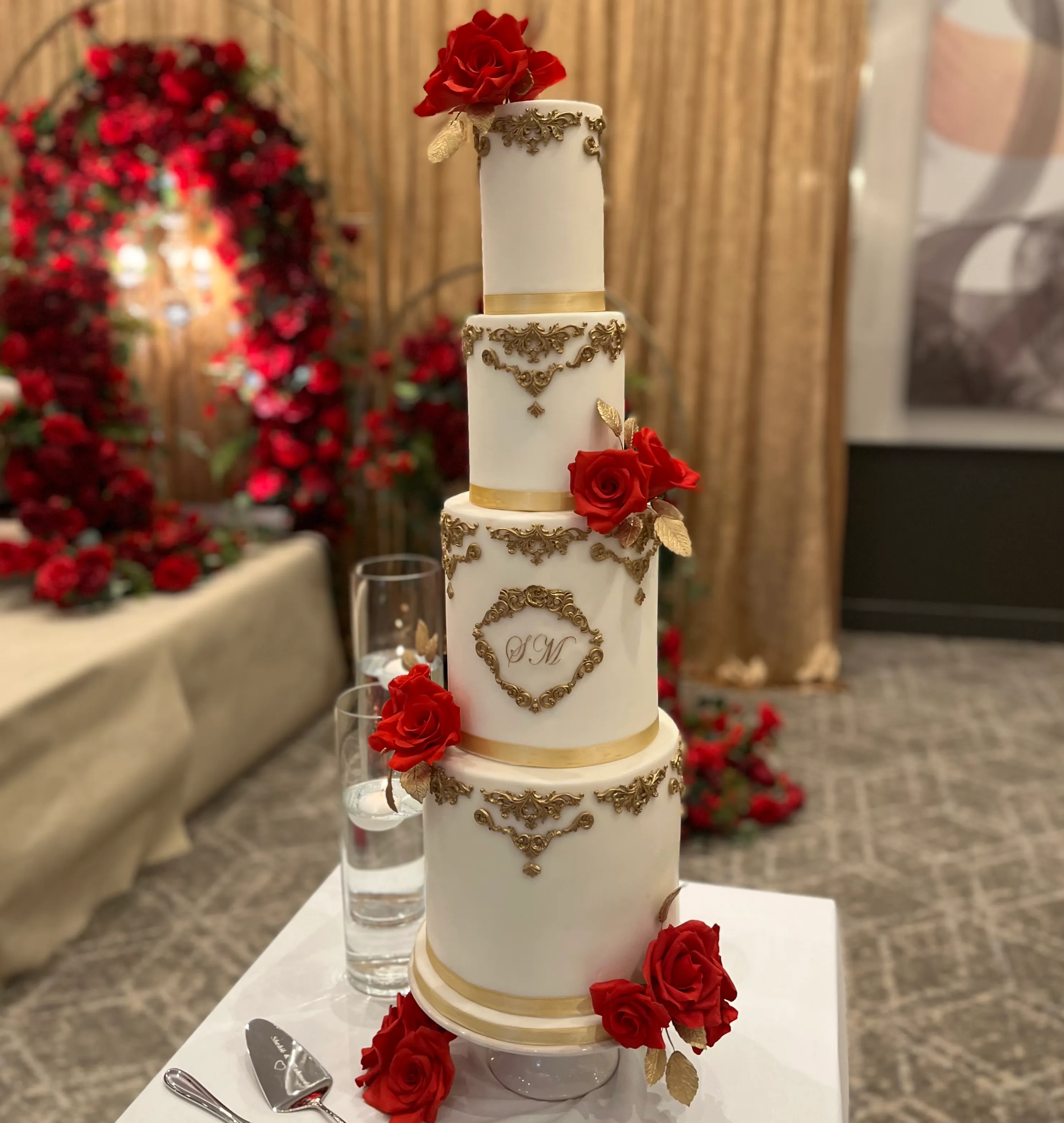 Four-tier white wedding cake with fresh white dahlias, burgundy roses, and cascading dark foliage with blackberry accents