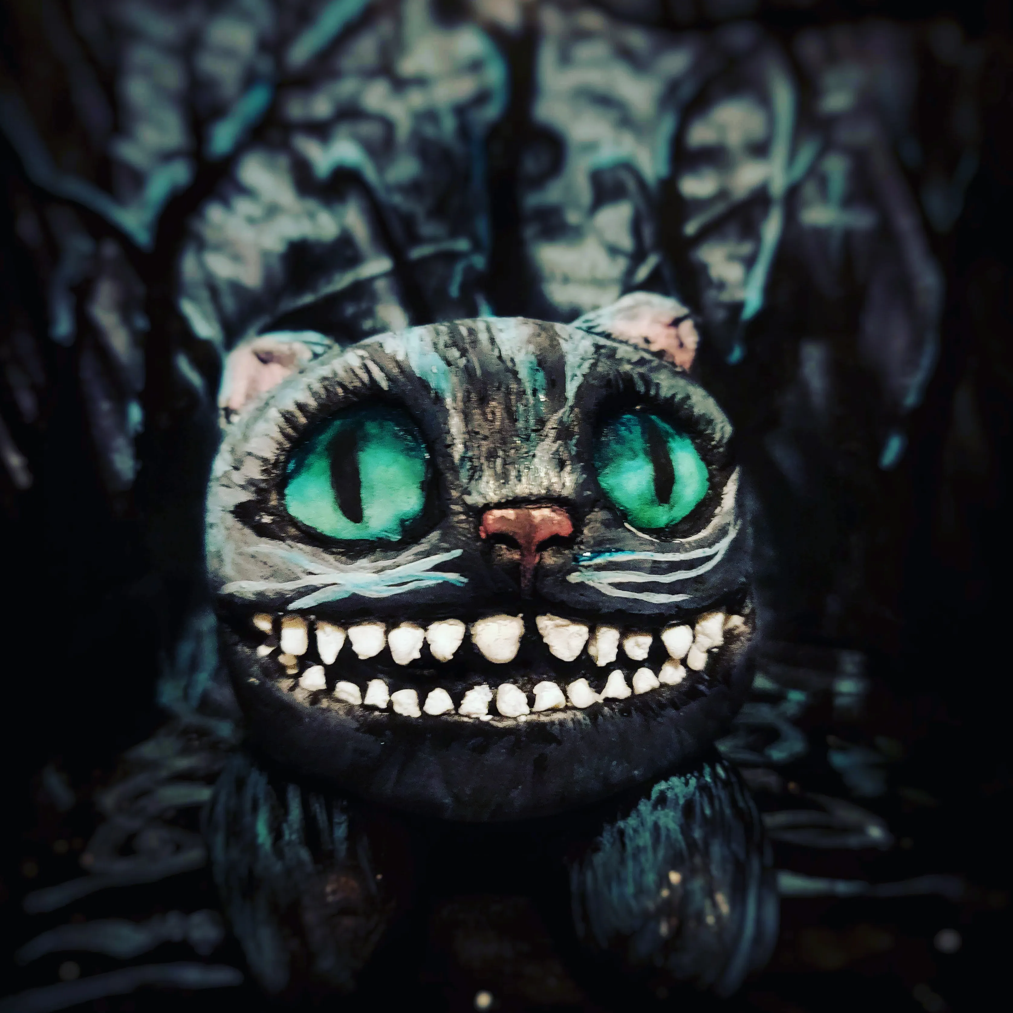 Sculpted Cheshire Cat with glowing green eyes and wide toothy grin against a dark forest backdrop