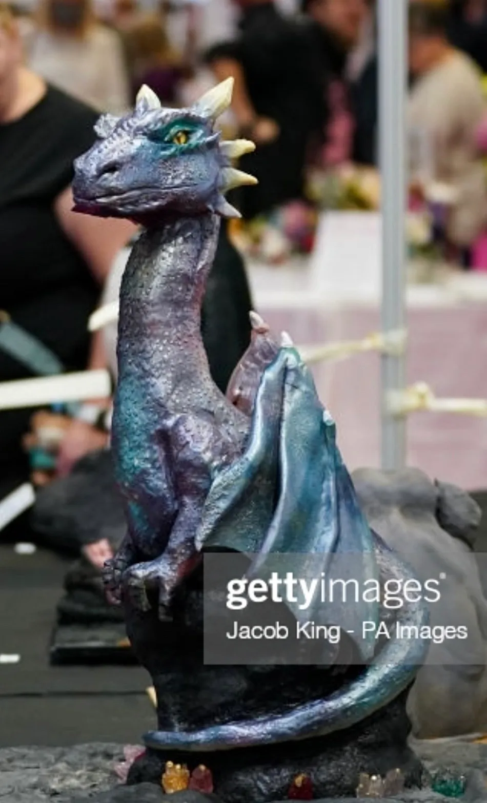Sculpted iridescent dragon in purple and teal with folded wings, horns and yellow eyes at a cake competition