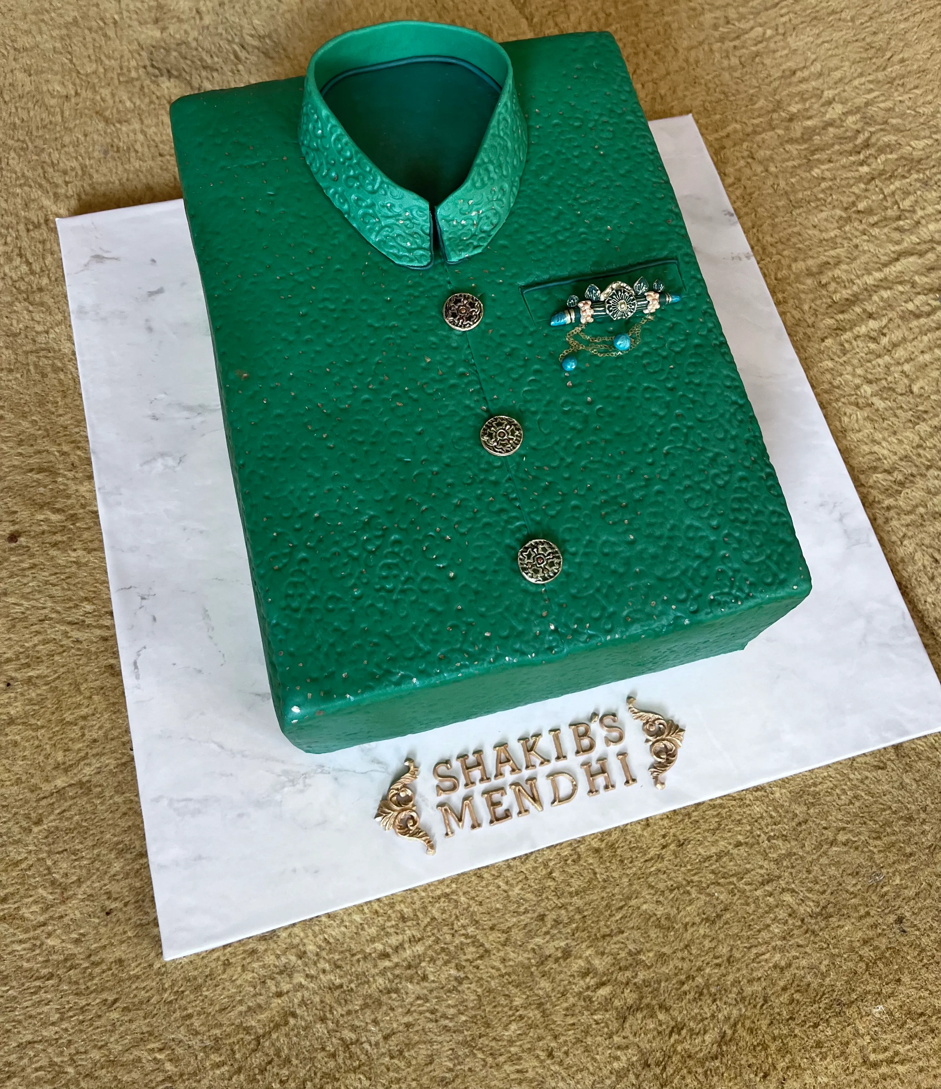 Sculpted green sherwani cake with ornate embossed fabric texture, metallic buttons and decorative brooch