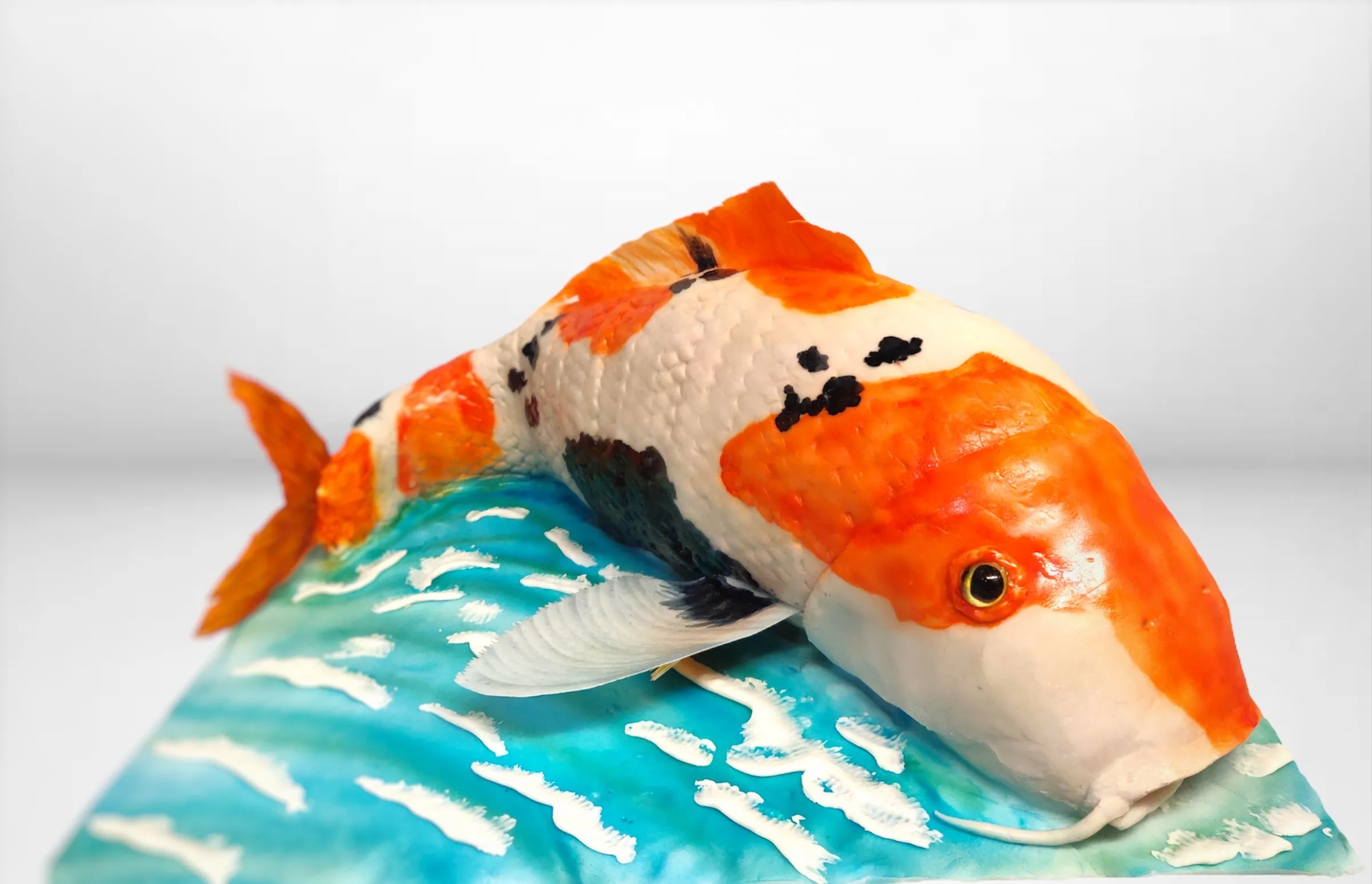 Sculpted koi fish in orange, white and black leaping over a turquoise water base with wave details