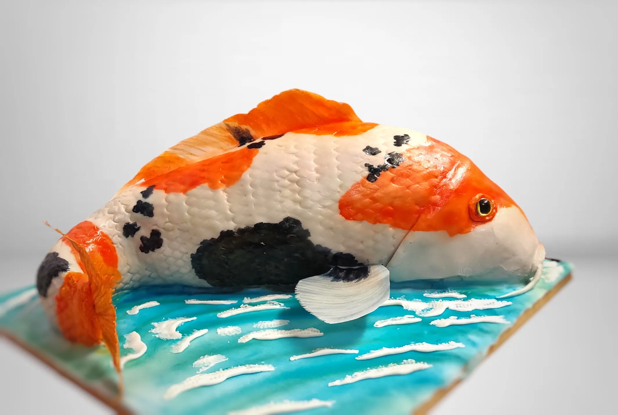 Sculpted koi fish cake side view showing the full leaping pose over a water base