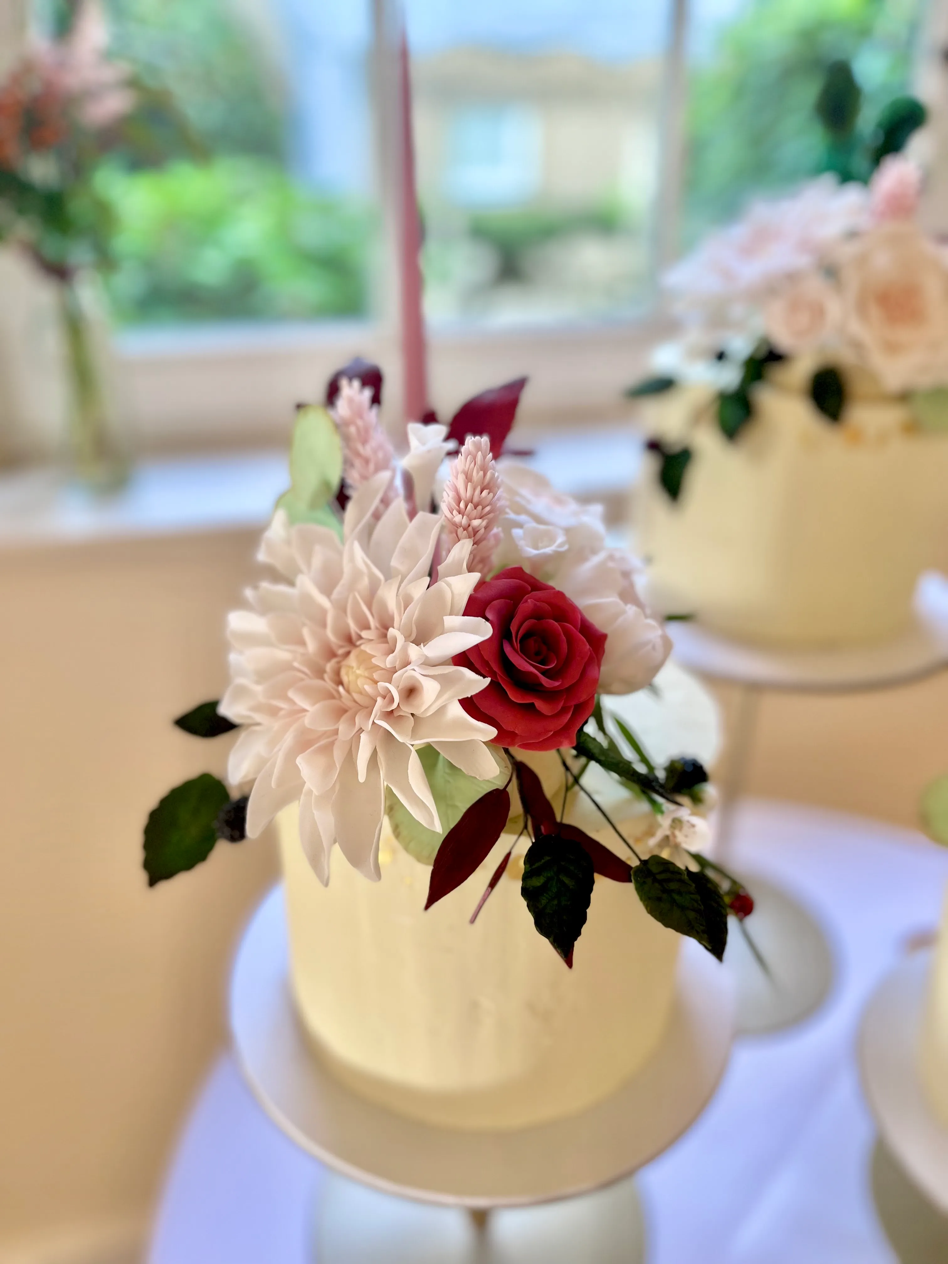 Multiple single-tier wedding cakes with cream frosting and pale pink and burgundy floral tops