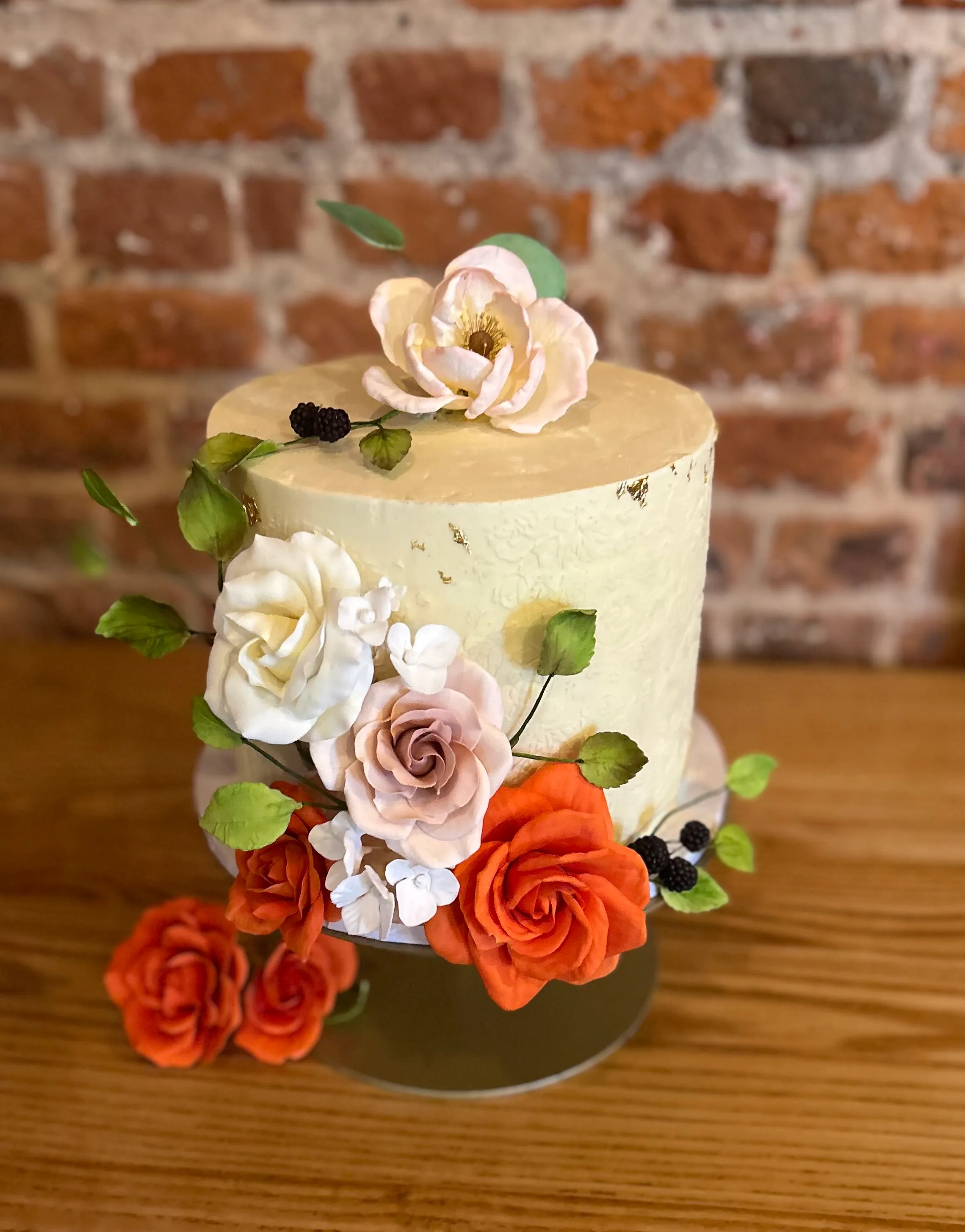 Single-tier pale yellow cake with cream and orange roses and green foliage