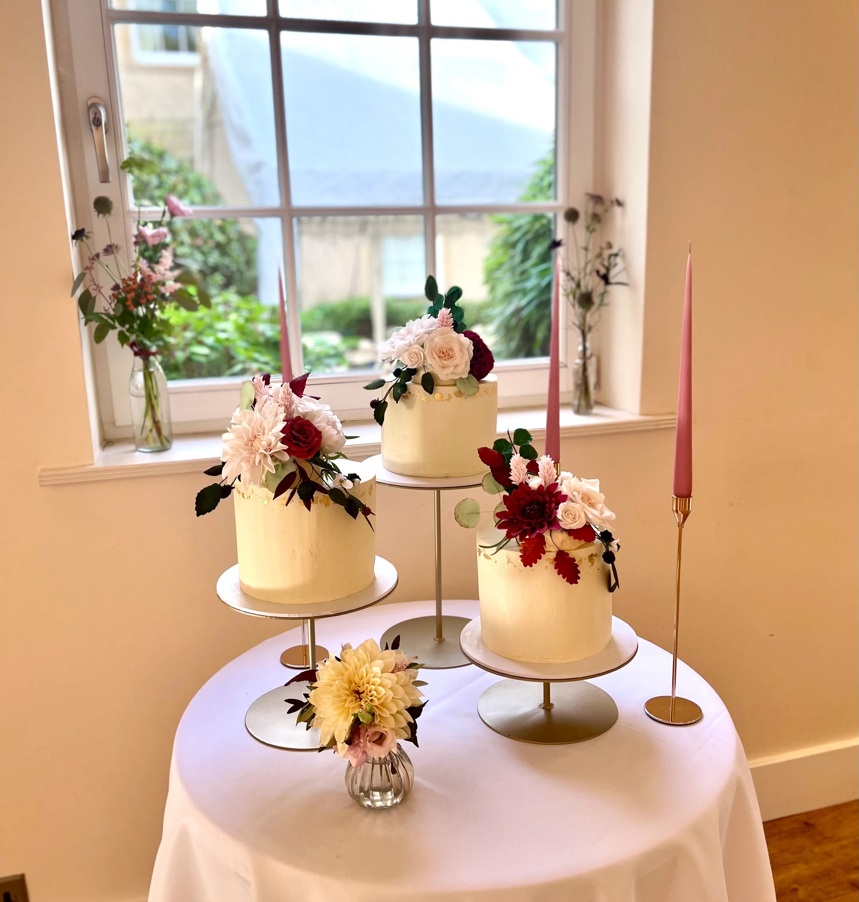 Trio of wedding cakes with burgundy dahlias and foliage on a styled table setting