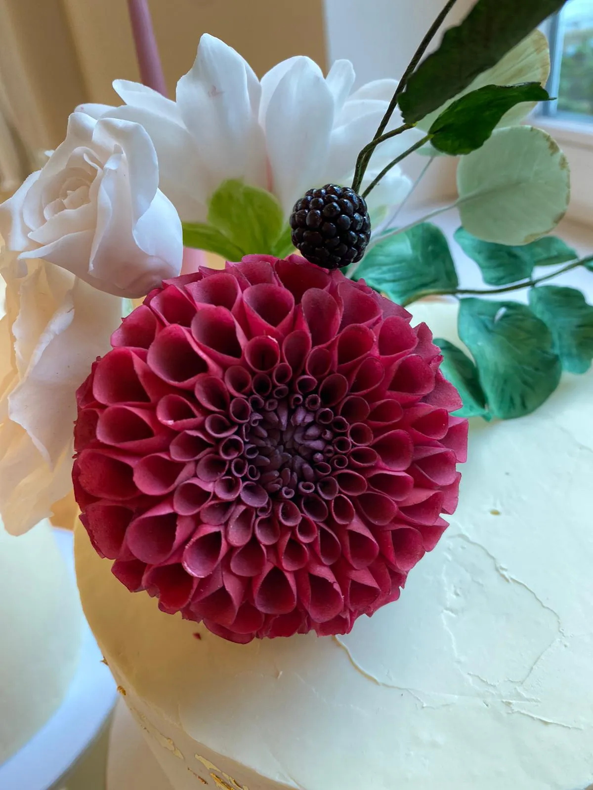 Two-tier white cake with bold fuchsia dahlia, white roses, and peach peonies